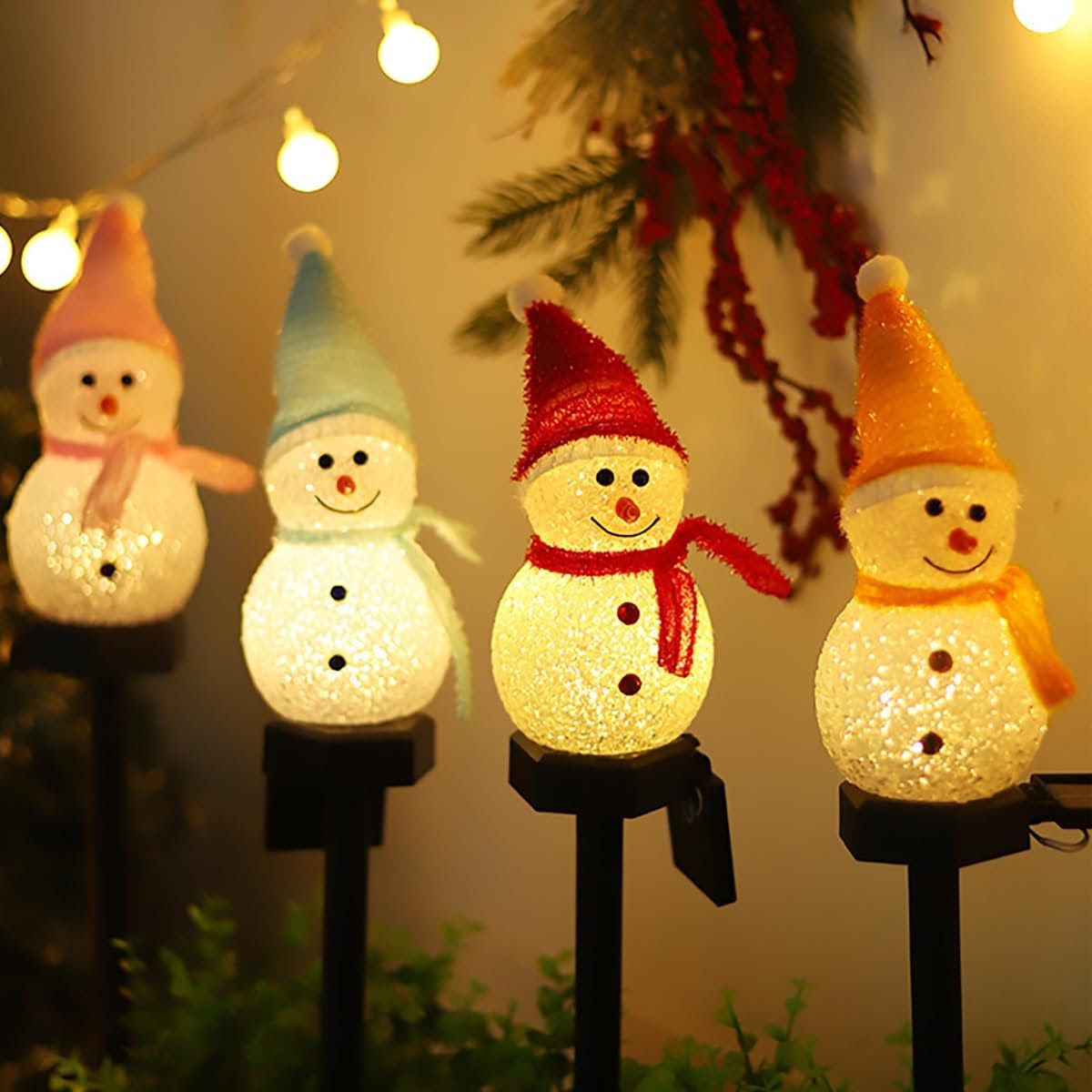 Close-up of four lit solar snowman Christmas pathway lights in pink, blue, red, and orange hats with warm white glow