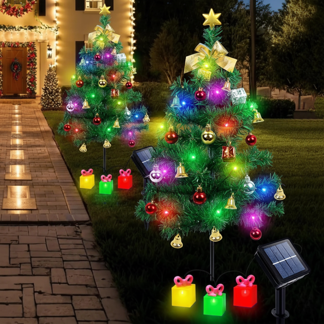 Two solar Christmas tree garden lights fully decorated with ornament bells and multicolor LEDs in front yard at night