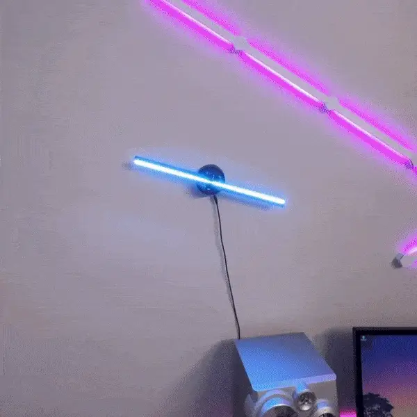 LED hologram fan wall-mounted in a dark gaming room displaying a blue and purple anime character hologram, purple neon strip light on ceiling
