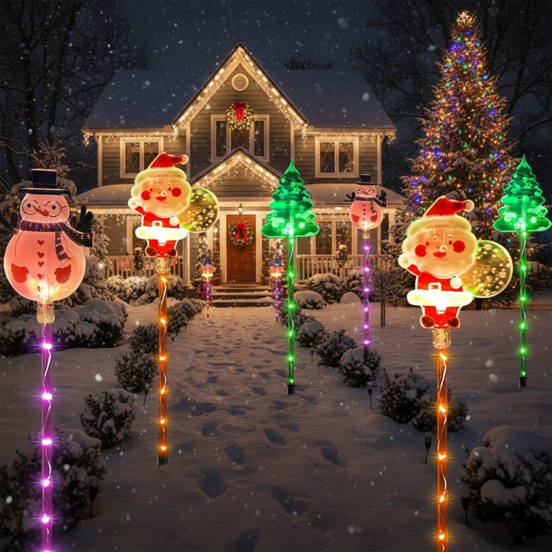 Pack of 6 solar Christmas moving lights with glowing Santa and snowman figures staked across a snow-covered yard in front of a decorated house