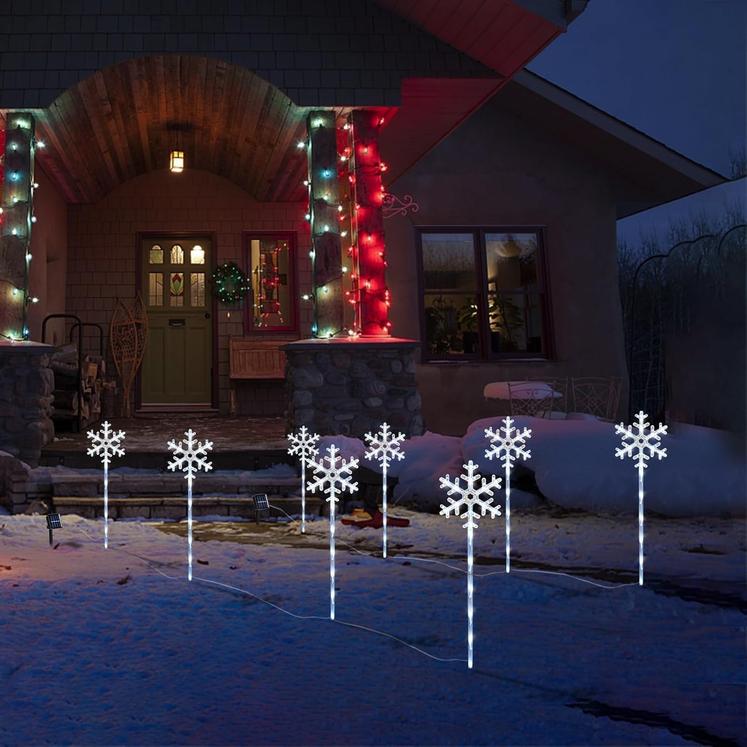 Eight solar snowflake pathway lights lined along a snowy front yard at night, white LED stakes glowing against a holiday-decorated home