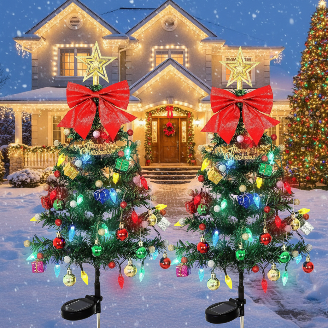 Two solar Christmas tree yard decorations with multicolor LED lights, red bow topper, star, and ornaments, displayed in front of a snow-covered house exterior with a set of 2
