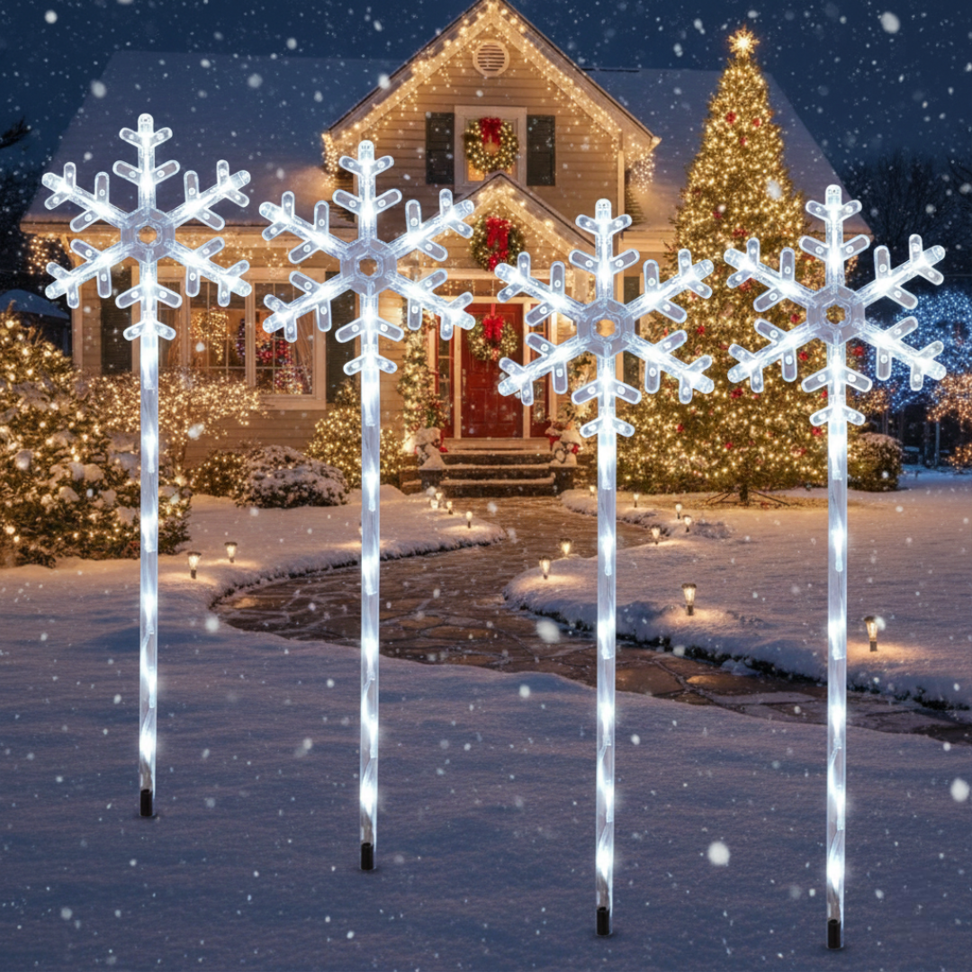 Four solar snowflake path lights with cool white LED stakes in snow, daytime view showing full-size snowflake silhouettes against a holiday home