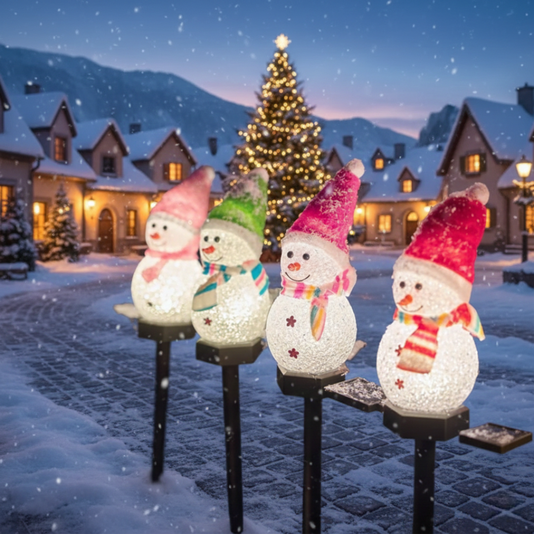 Four solar snowman Christmas pathway lights in colorful hats glowing in a snowy village square at night