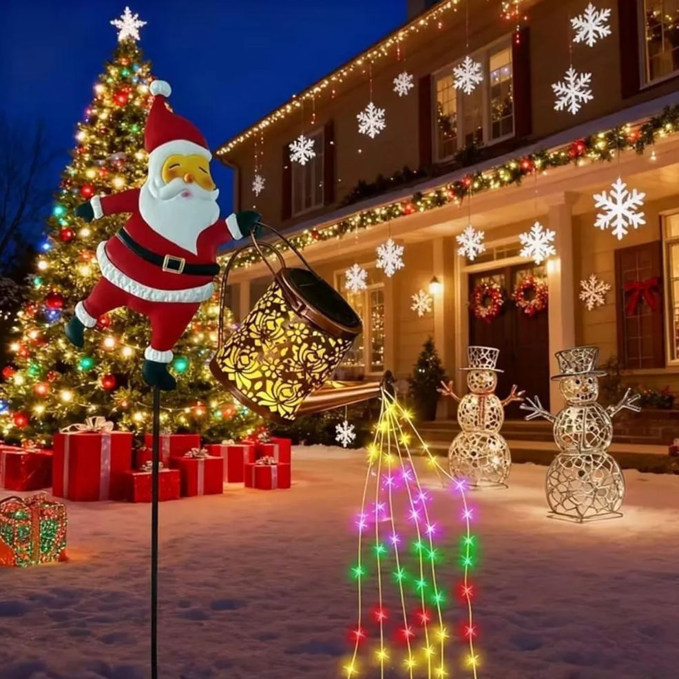 Solar Santa kettle garden stake light placed in a snowy front yard next to snowmen with LED strands cascading from the copper watering can