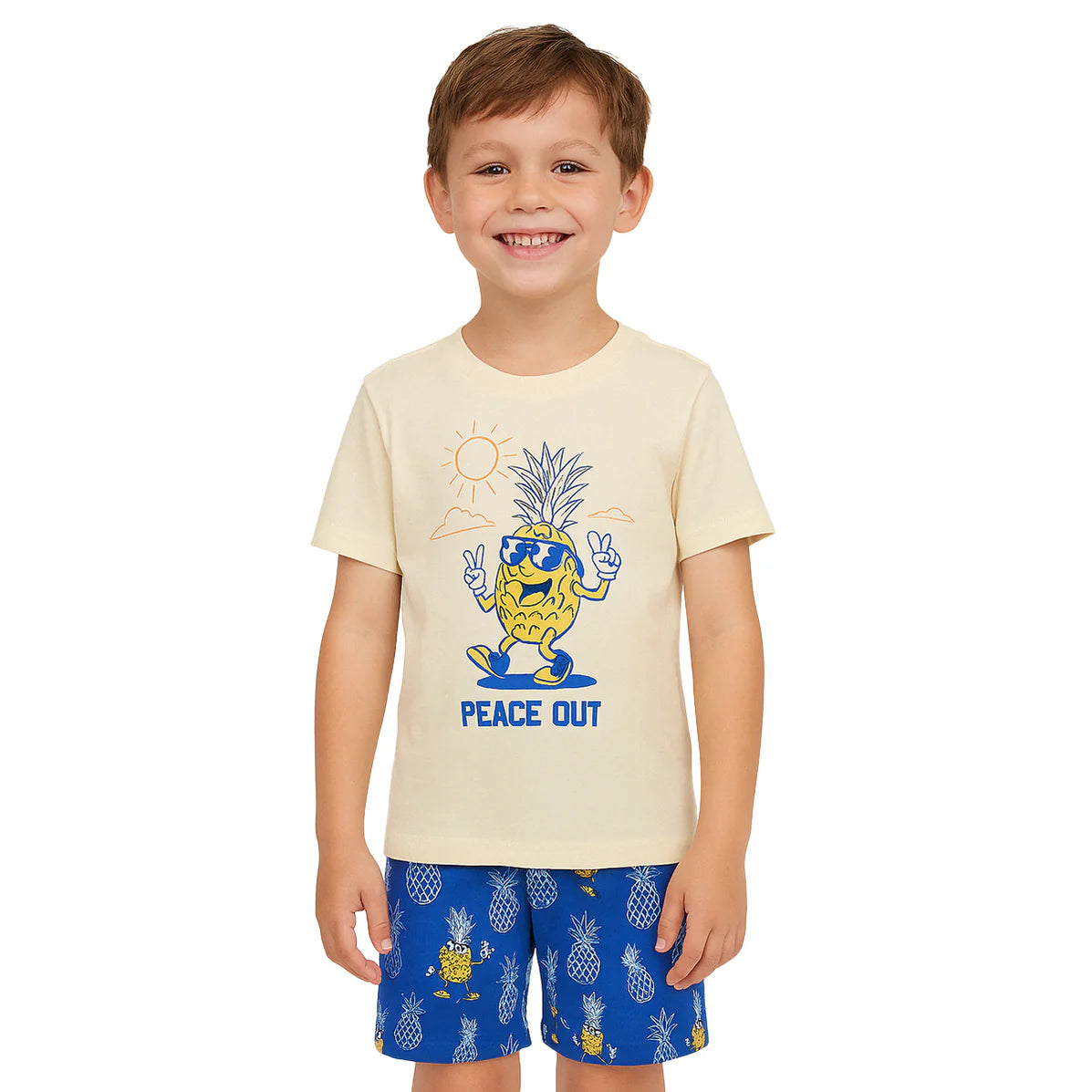 Smiling young boy wearing a beige t-shirt with a cartoon pineapple and 'Peace Out' graphic, paired with blue shorts featuring pineapple prints.