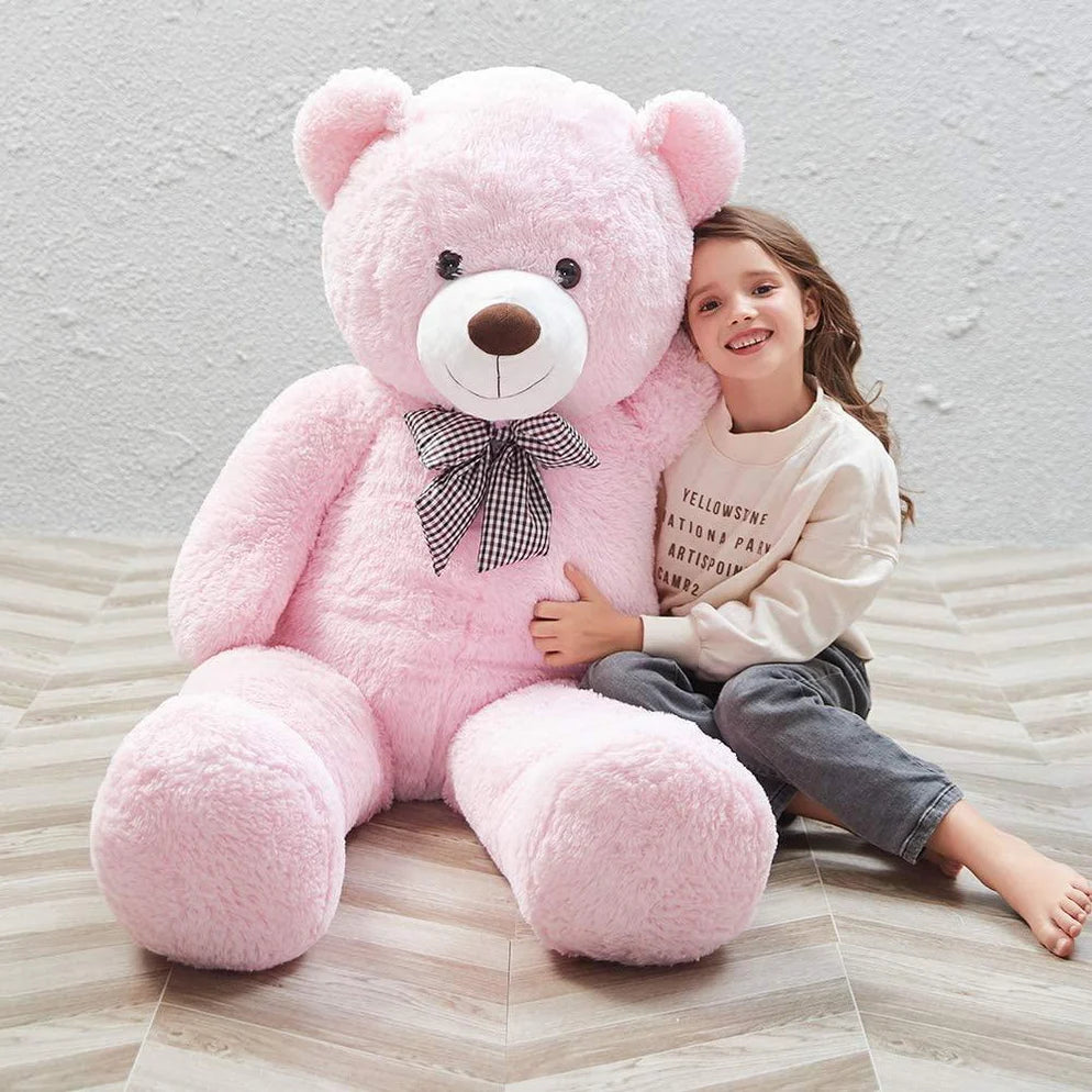 A young girl sitting and hugging a fluffy pink teddy bear on a wooden floor.