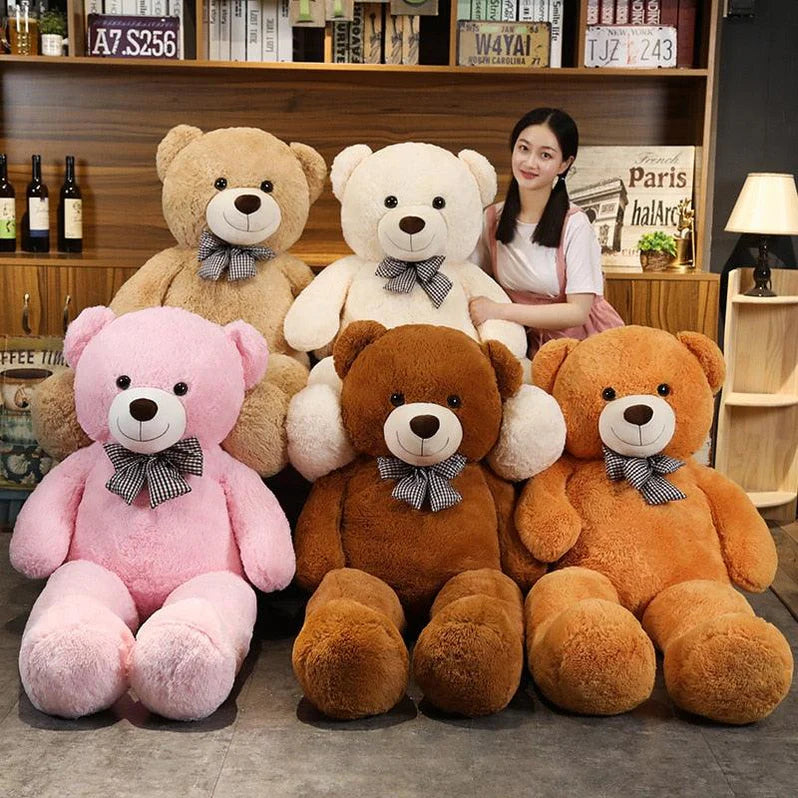 A woman posing with six giant teddy bears in various colors, seated in a home setting.