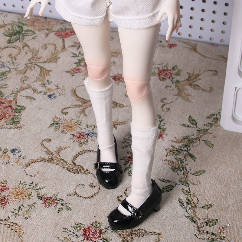 BJD doll wearing black patent Mary Jane shoes with white socks on floral carpet