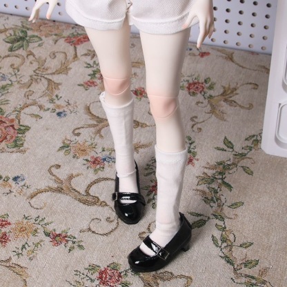 BJD doll wearing black patent Mary Jane shoes with white socks on floral carpet
