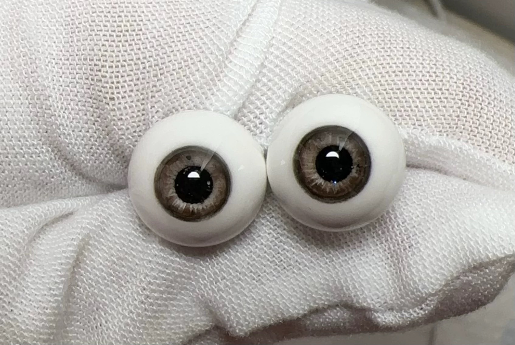 Realistic brown glass eyes for 1/3 BJD dolls resting on a white gloved hand - Atelier Chantilly