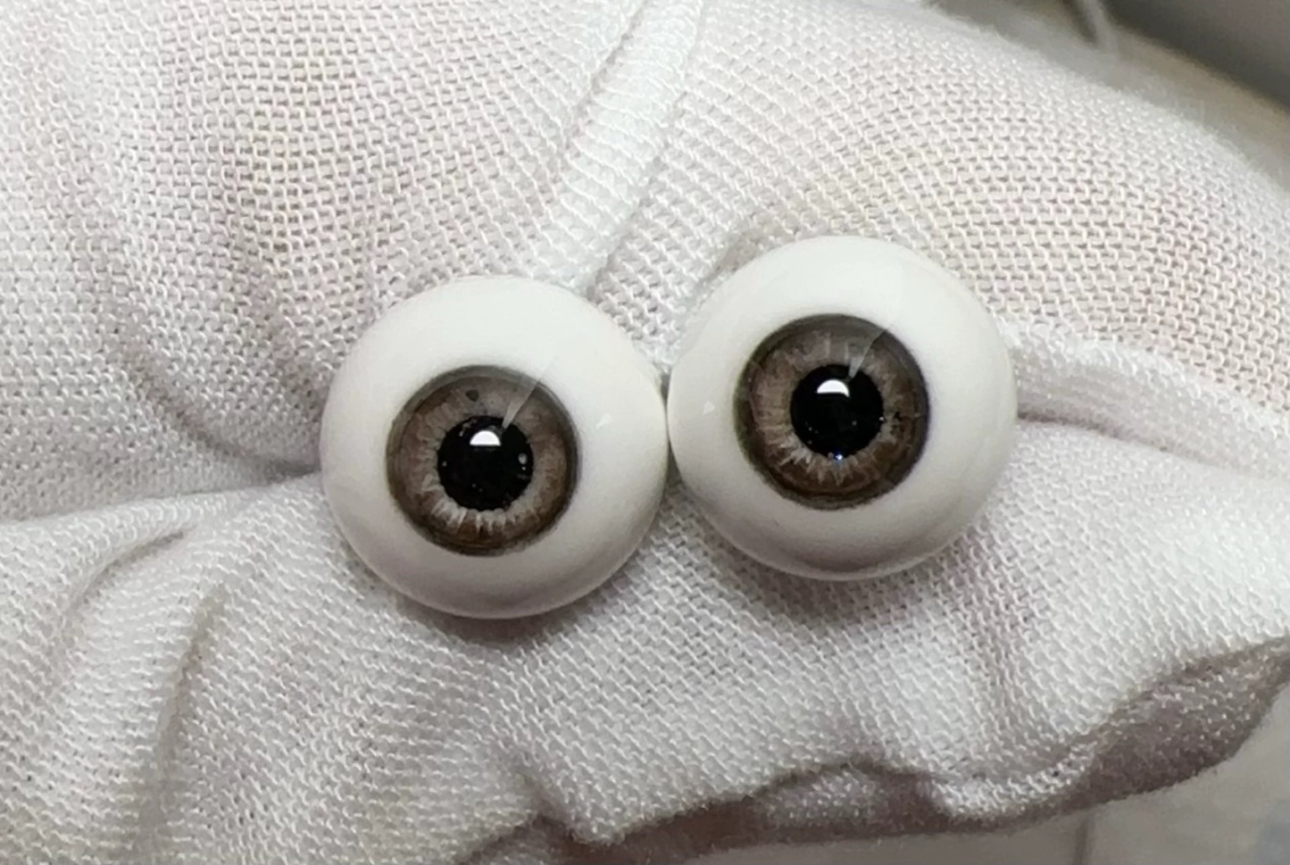 Realistic brown glass eyes for 1/3 BJD dolls resting on a white gloved hand - Atelier Chantilly