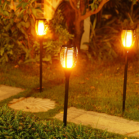 Three solar flame flickering torches staked along a garden path at night
