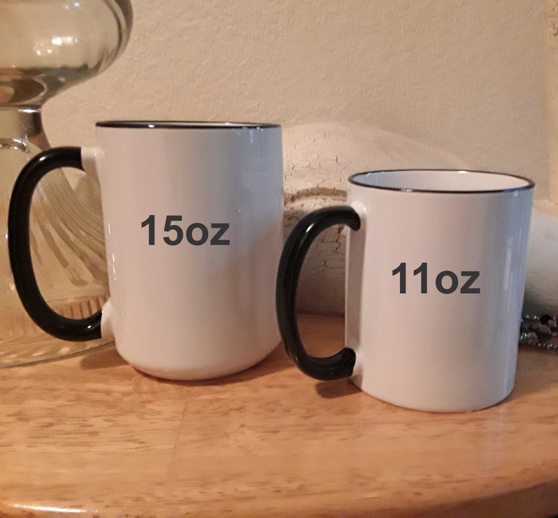 May include: Two white ceramic mugs with black handles and black rims. The larger mug is 15oz and the smaller mug is 11oz.