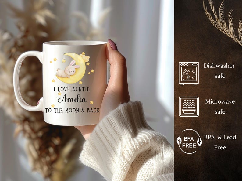 May include: White ceramic mug with a yellow moon and a bunny sleeping on it. The mug has the text "I love Auntie Amedia to the moon & back" printed on it.
