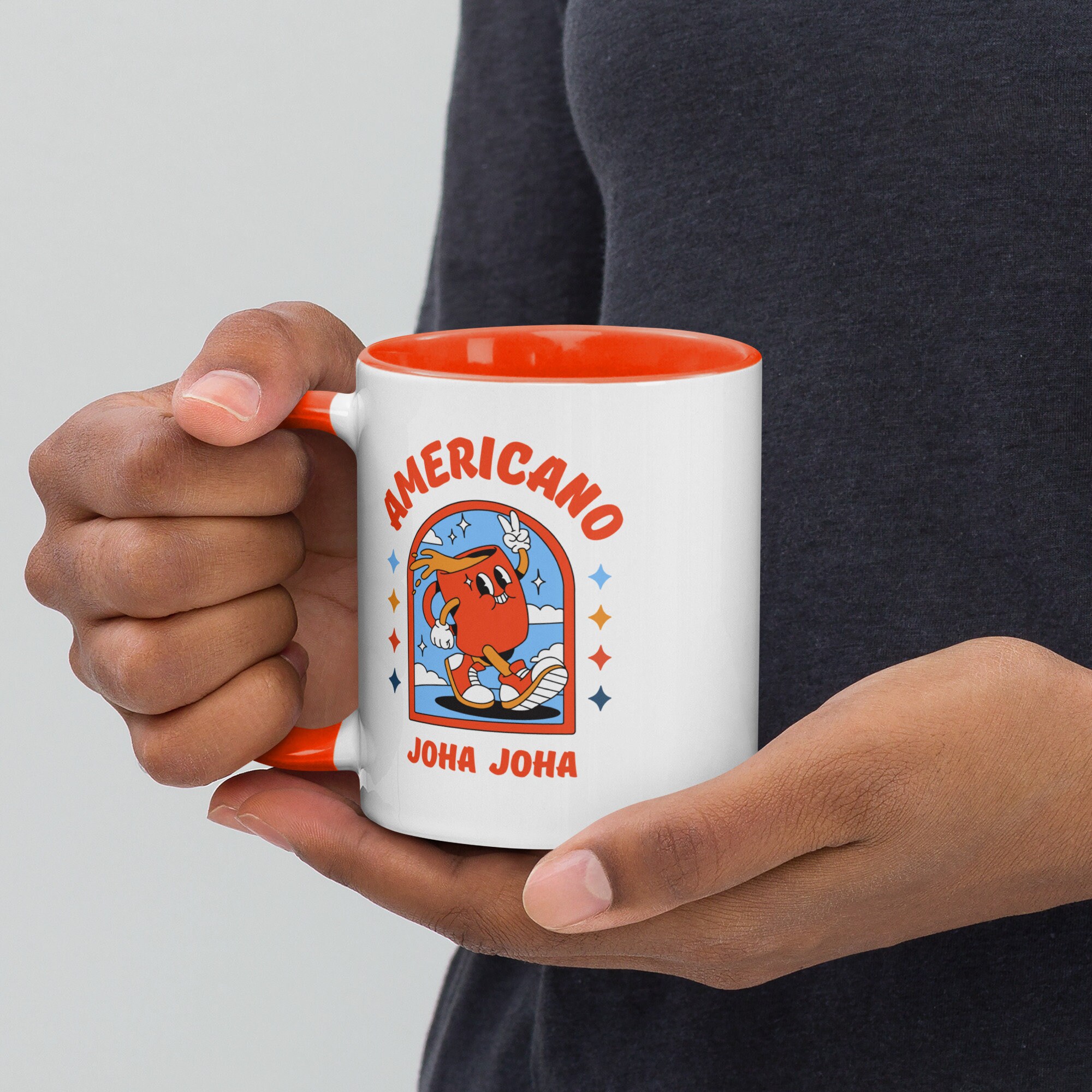 Person holding a ceramic coffee mug featuring a retro cartoon coffee character with Americano Joha Joha text and orange interior