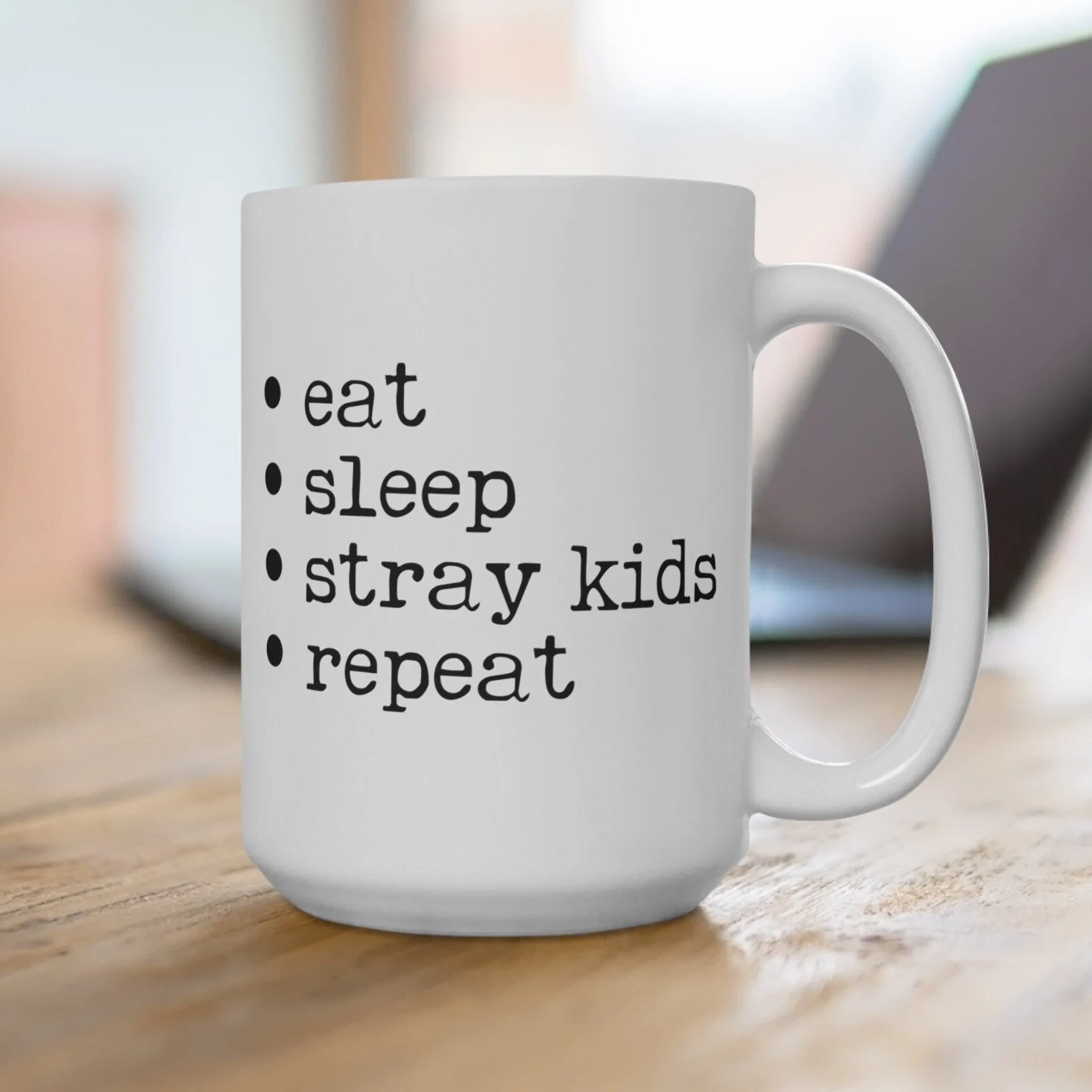 White ceramic coffee mug with black text reading eat sleep stray kids repeat in a checklist format on a wooden table