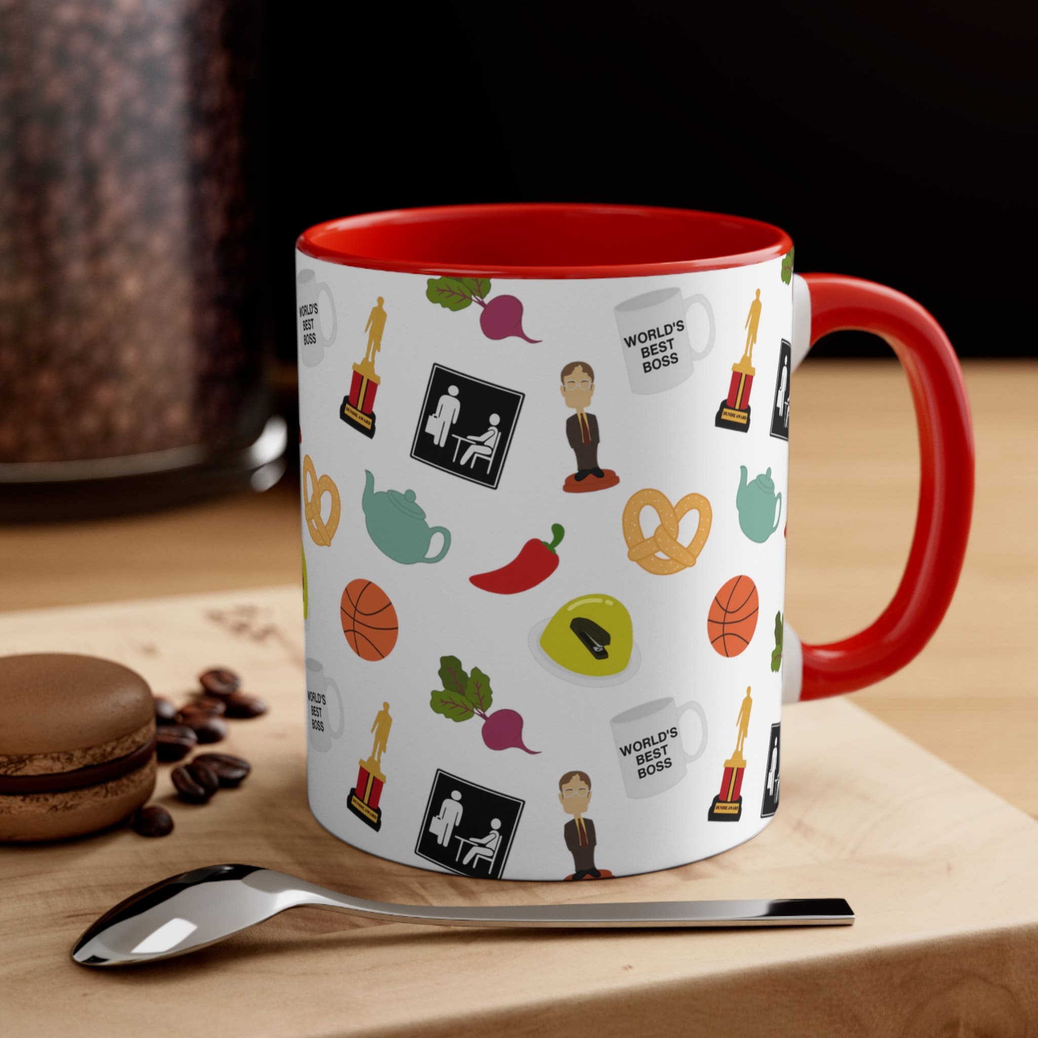 Ceramic coffee mug with a white exterior featuring a pattern of icons from The Office including a Dundie award, teapot, and Dwight bobblehead with a red interior and handle.