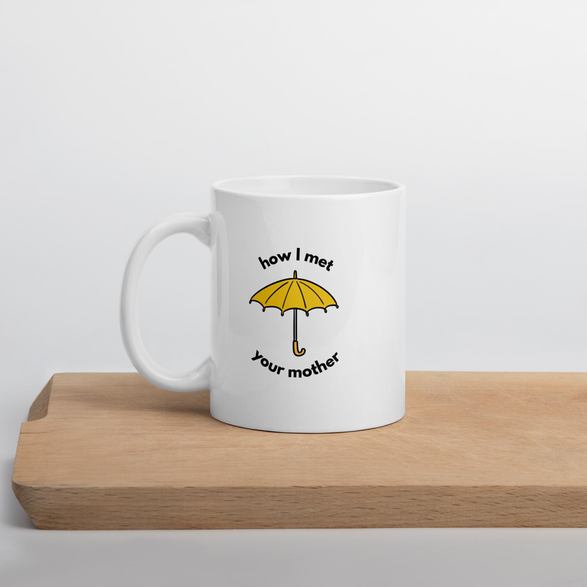 Side view of a white ceramic mug with the yellow umbrella graphic sitting on a wooden cutting board