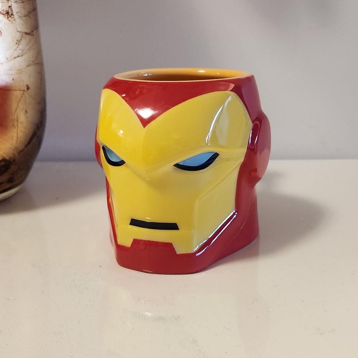 Three dimensional sculpted ceramic mug in the shape of Iron Man helmet with yellow faceplate and blue eyes