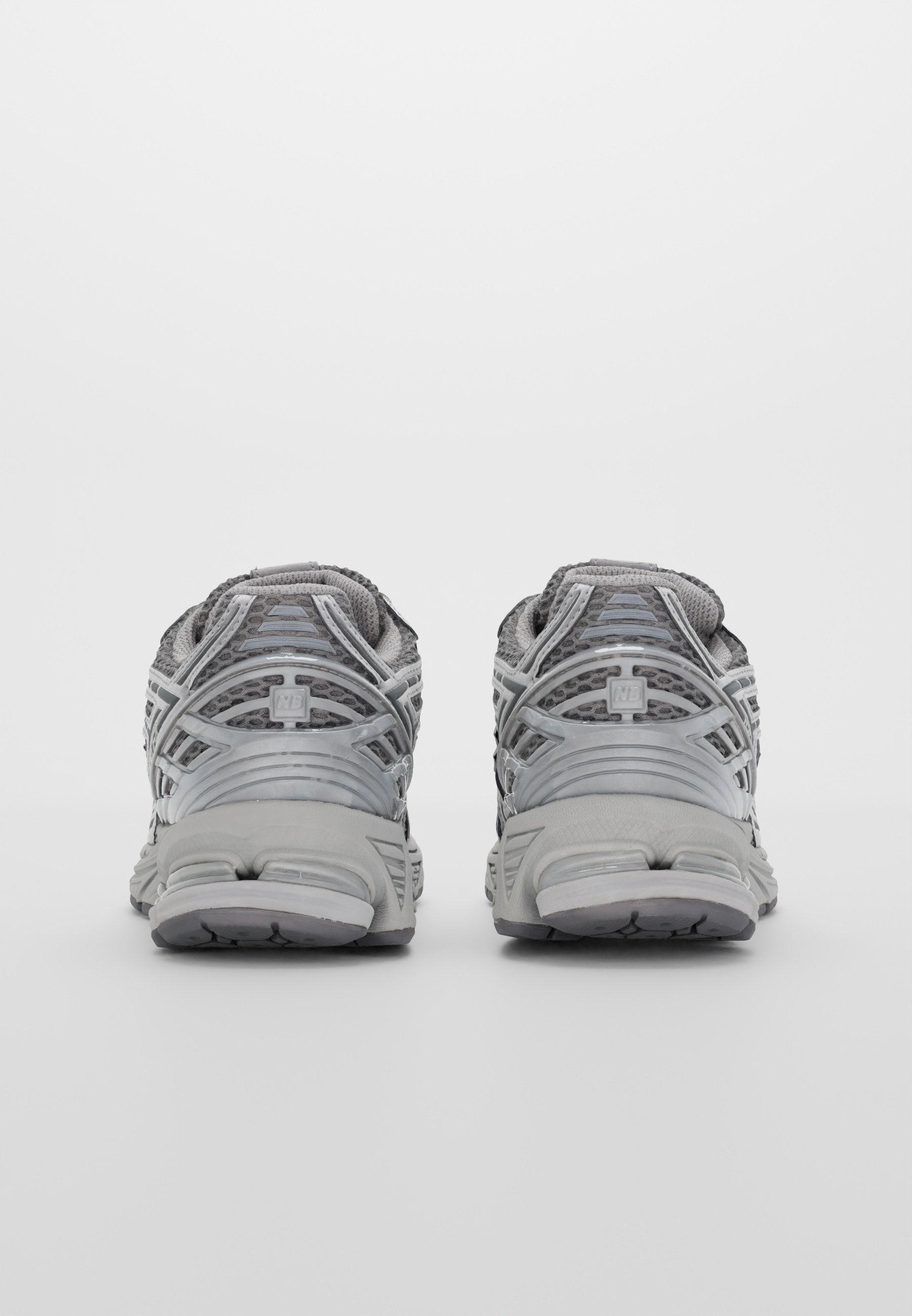 Zapatillas deportivas grises con una parte superior de malla y superposiciones reforzadas, talón acolchado y suela de goma texturizada. La vista trasera destaca los detalles del diseño.