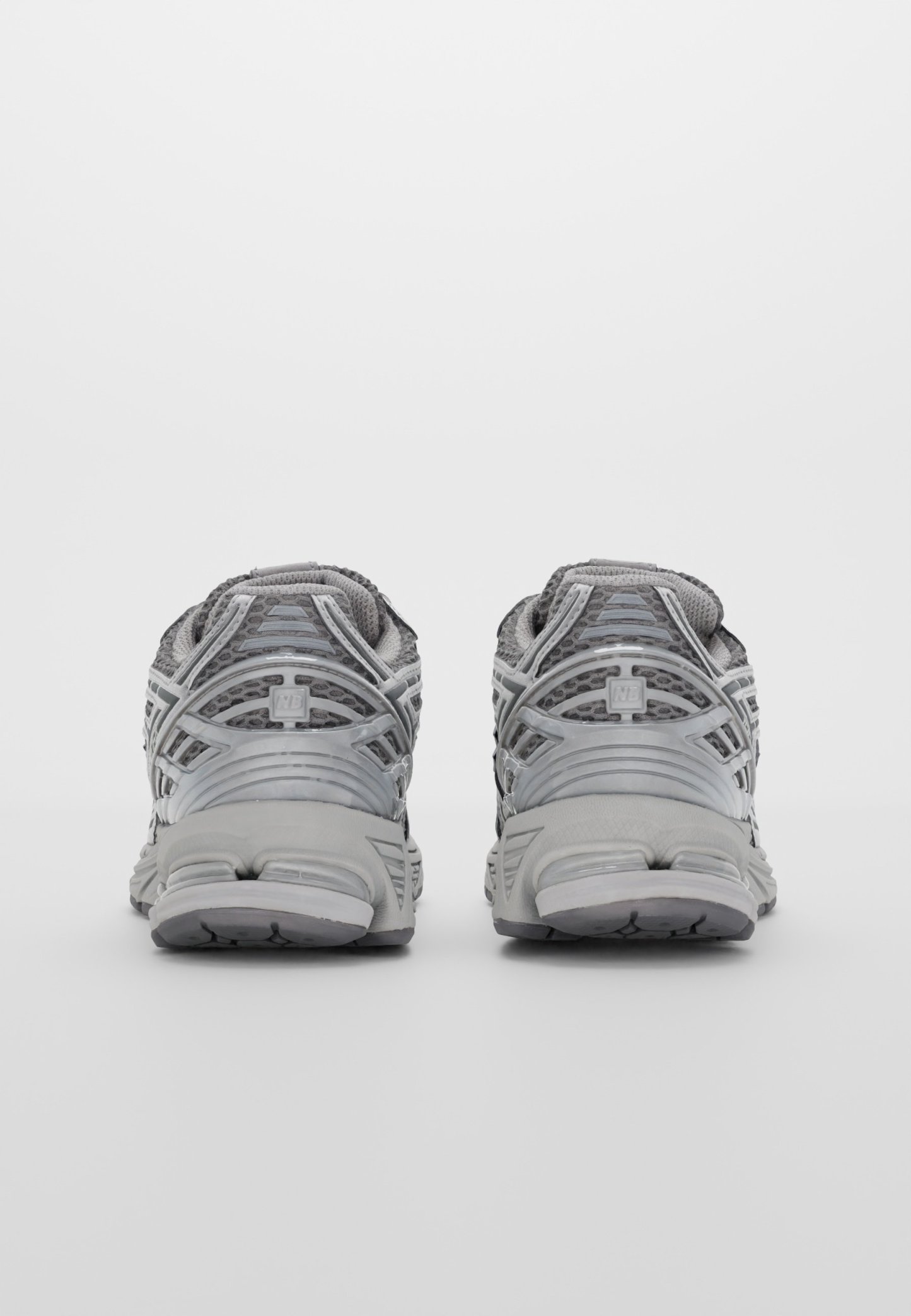 Zapatillas deportivas grises con una parte superior de malla y superposiciones reforzadas, talón acolchado y suela de goma texturizada. La vista trasera destaca los detalles del diseño.
