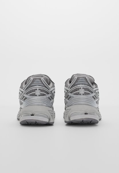 Zapatillas deportivas grises con una parte superior de malla y superposiciones reforzadas, talón acolchado y suela de goma texturizada. La vista trasera destaca los detalles del diseño.