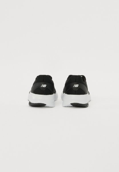 Zapatillas deportivas negras con parte superior de malla, suelas de goma blancas y un logotipo distintivo en el talón, con un diseño texturizado.