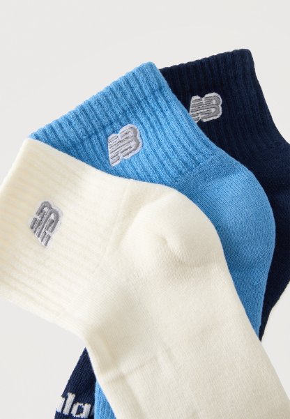Tres pares de calcetines tobilleros acanalados en blanco, azul claro y azul marino, cada uno con un pequeño logo bordado cerca del puño.