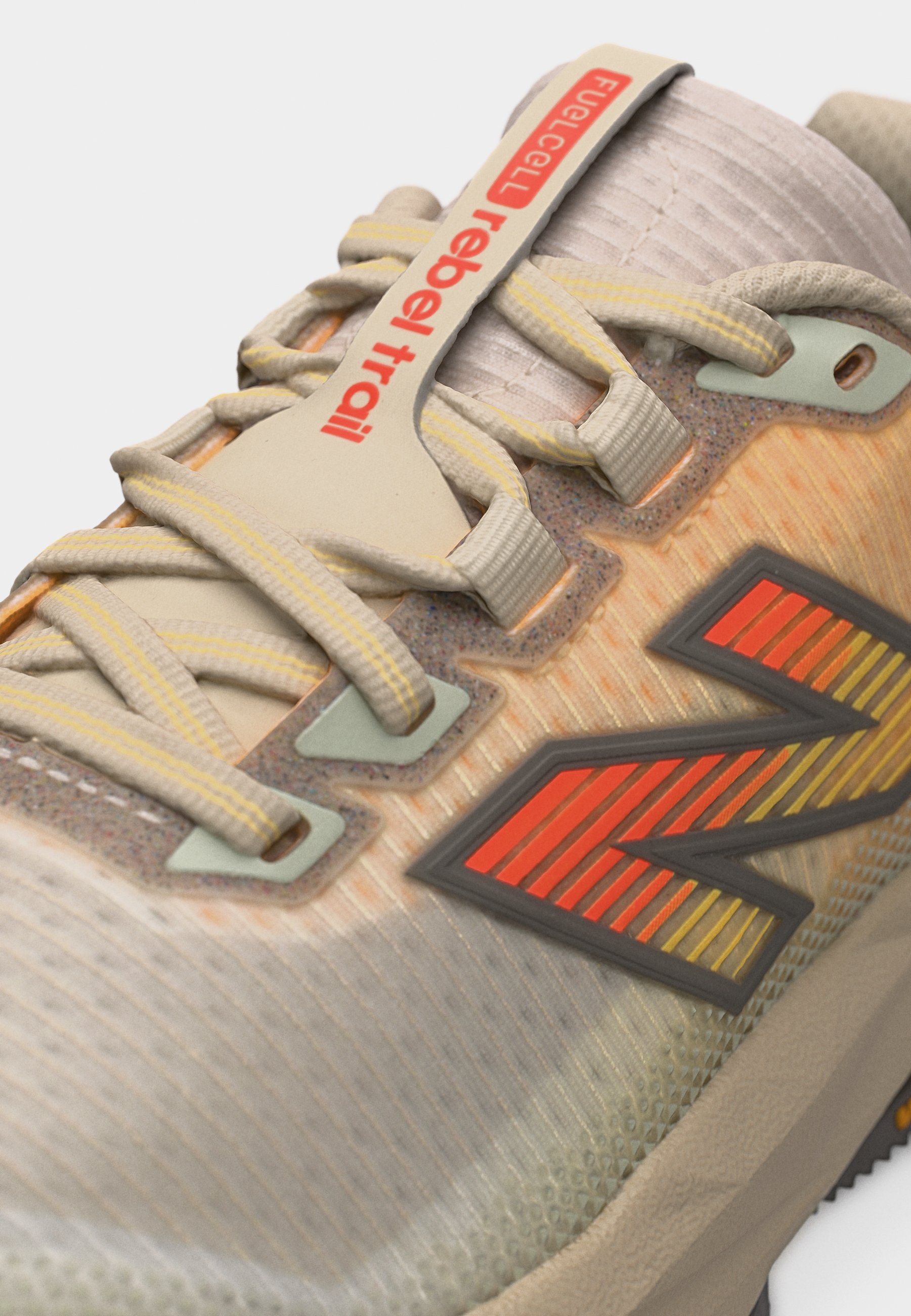 Primer plano de zapatilla de trail running beige con cordones con acentos amarillos, vibrante logo "N" naranja y texto "FuelCell rebel trail" en la lengüeta.