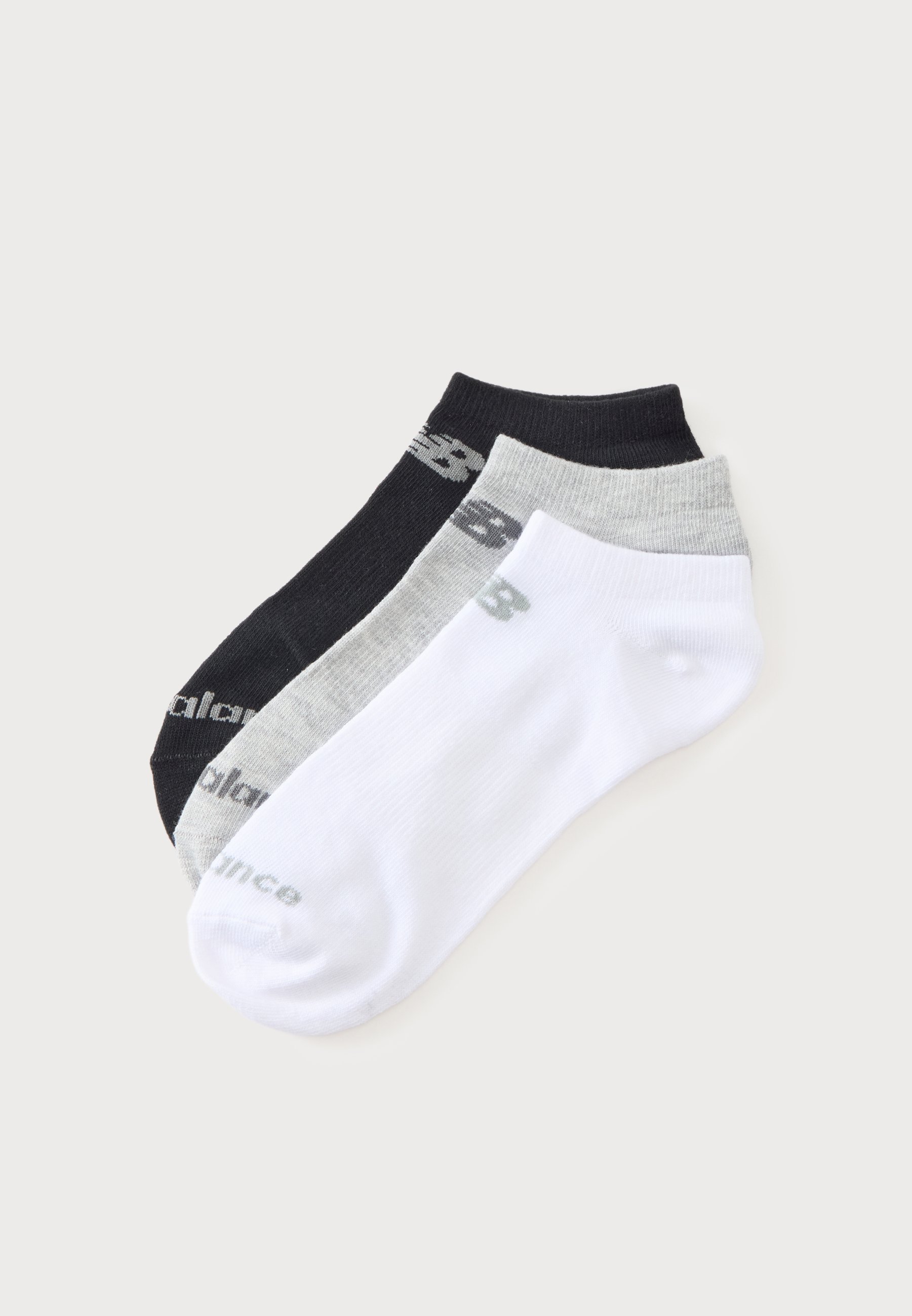 Tres calcetines tobilleros extendidos en negro, gris y blanco, cada uno con el logo "New Balance" en color contrastante cerca del puño y la puntera.