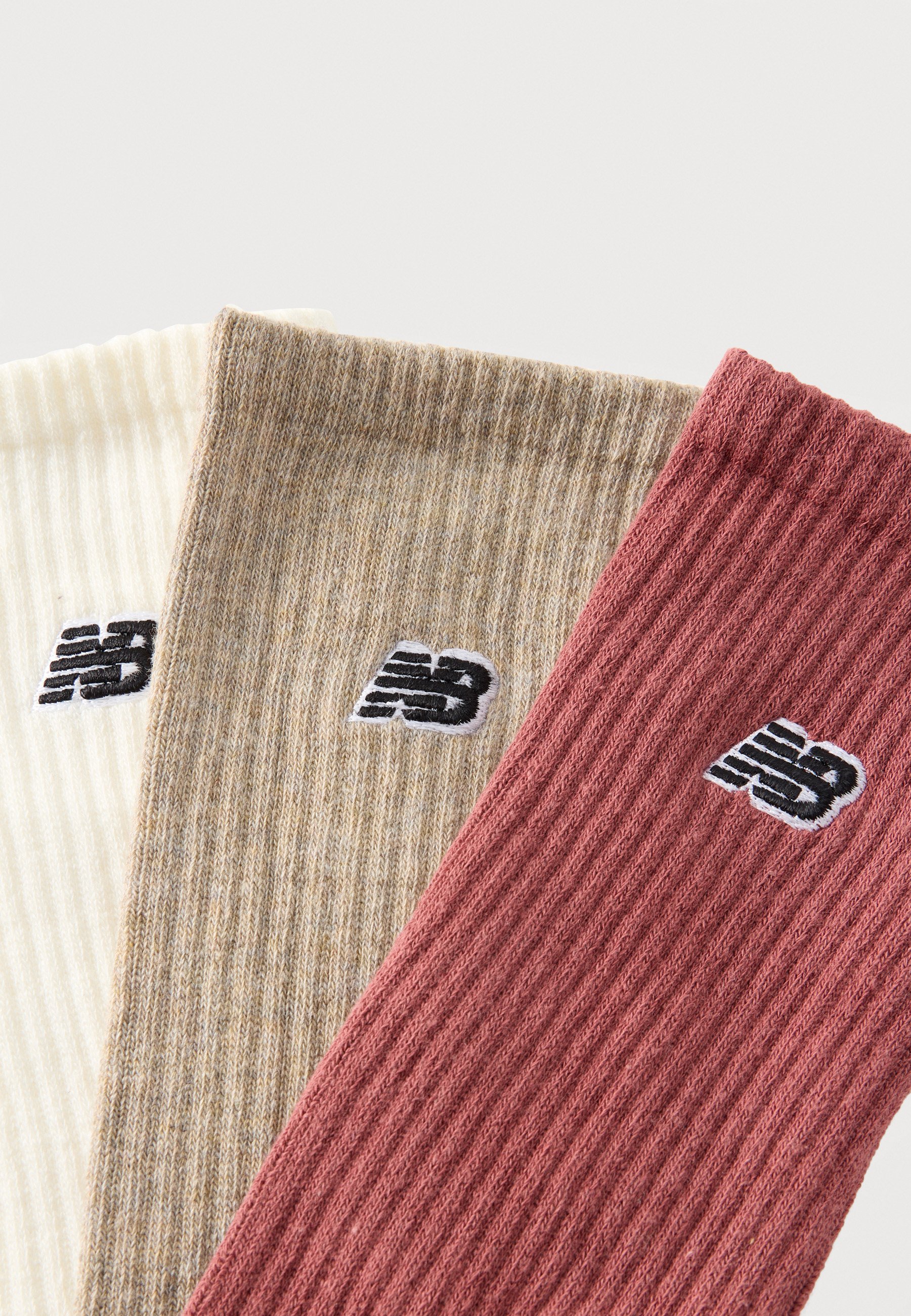 Tres calcetines de punto acanalado en crema, beige y rosa empolvado con logotipos "NB" en blanco y negro sobre un fondo blanco.