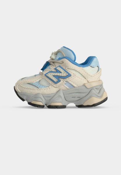 Zapatilla para niño pequeño en crema y azul claro con suela gris gruesa y logotipo "N" azul en el lateral, mostrada sobre un fondo blanco.