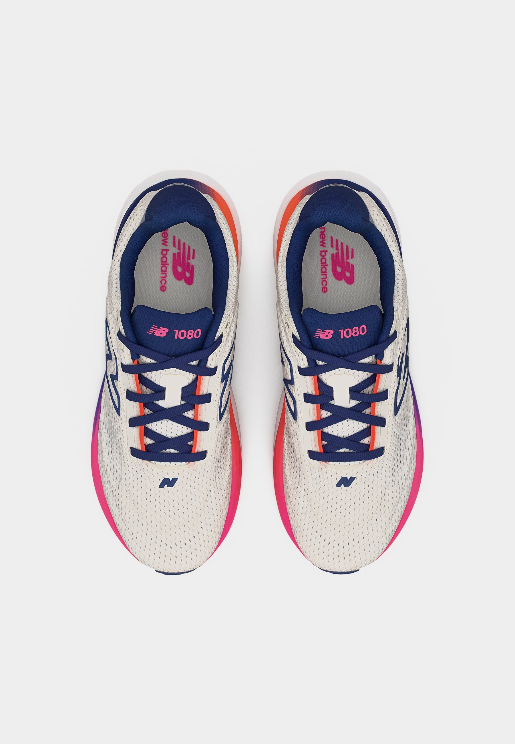 Par de zapatillas New Balance 1080 blancas con cordones azul marino y suelas con degradado rosa-naranja, vistas desde arriba sobre un fondo blanco.
