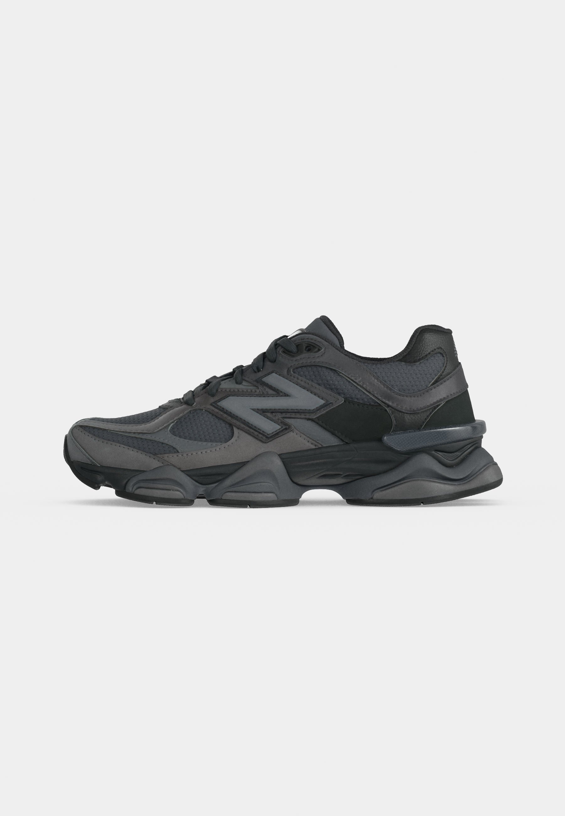 Zapatilla deportiva negra y gris oscuro con parte superior de malla y cuero, suela gruesa y logo lateral de marca, mostrada desde el lado exterior.