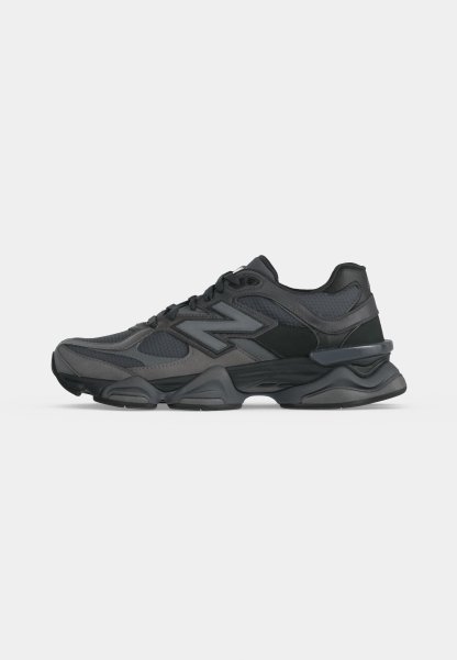 Zapatilla deportiva negra y gris oscuro con parte superior de malla y cuero, suela gruesa y logo lateral de marca, mostrada desde el lado exterior.