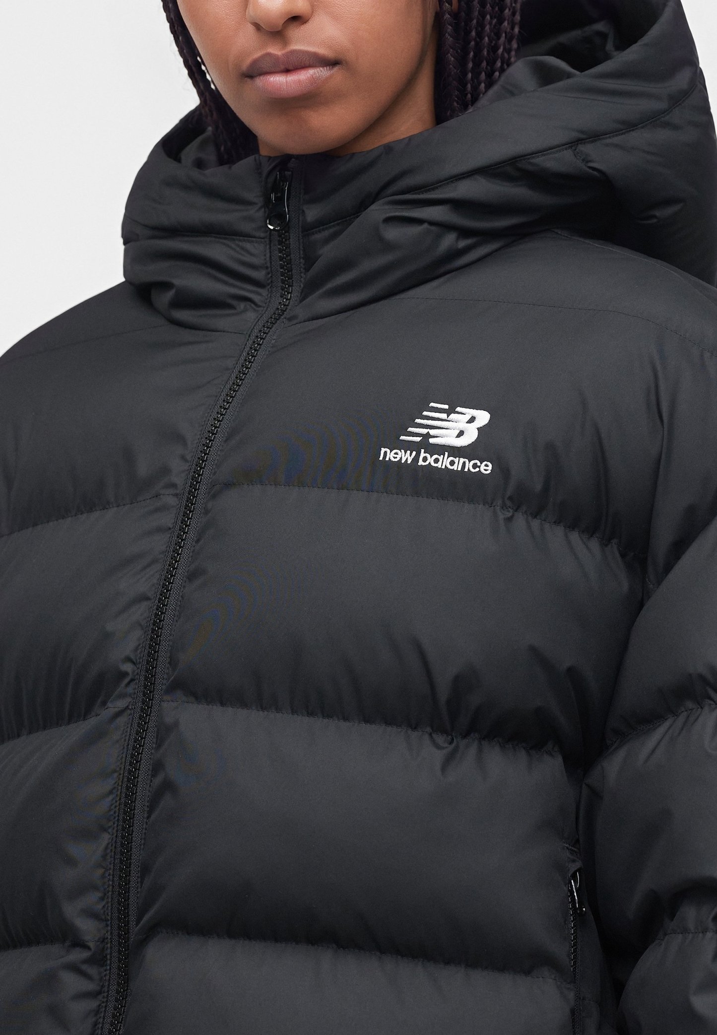 Primer plano de una persona que lleva una chaqueta acolchada negra de New Balance con cuello alto y capucha con cremallera.
