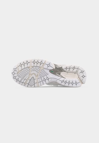 Suela de un zapato deportivo blanco y gris con un patrón de tracción de panal y cuadrícula sobre un fondo blanco liso.