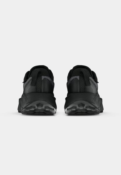 Zapatillas deportivas negras con parte superior texturizada, talón reforzado y suela negra gruesa con patrones de tracción. Dos tiradores traseros para ponerlas y quitarlas fácilmente.