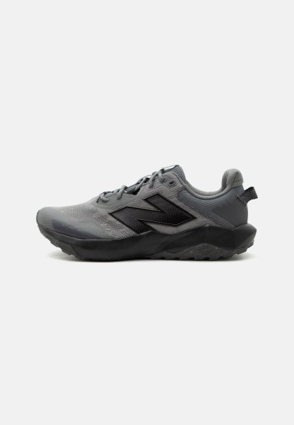 Zapatilla New Balance gris y negra con parte superior de malla, cierre de cordones, cuello acolchado y suela resistente para correr en senderos.