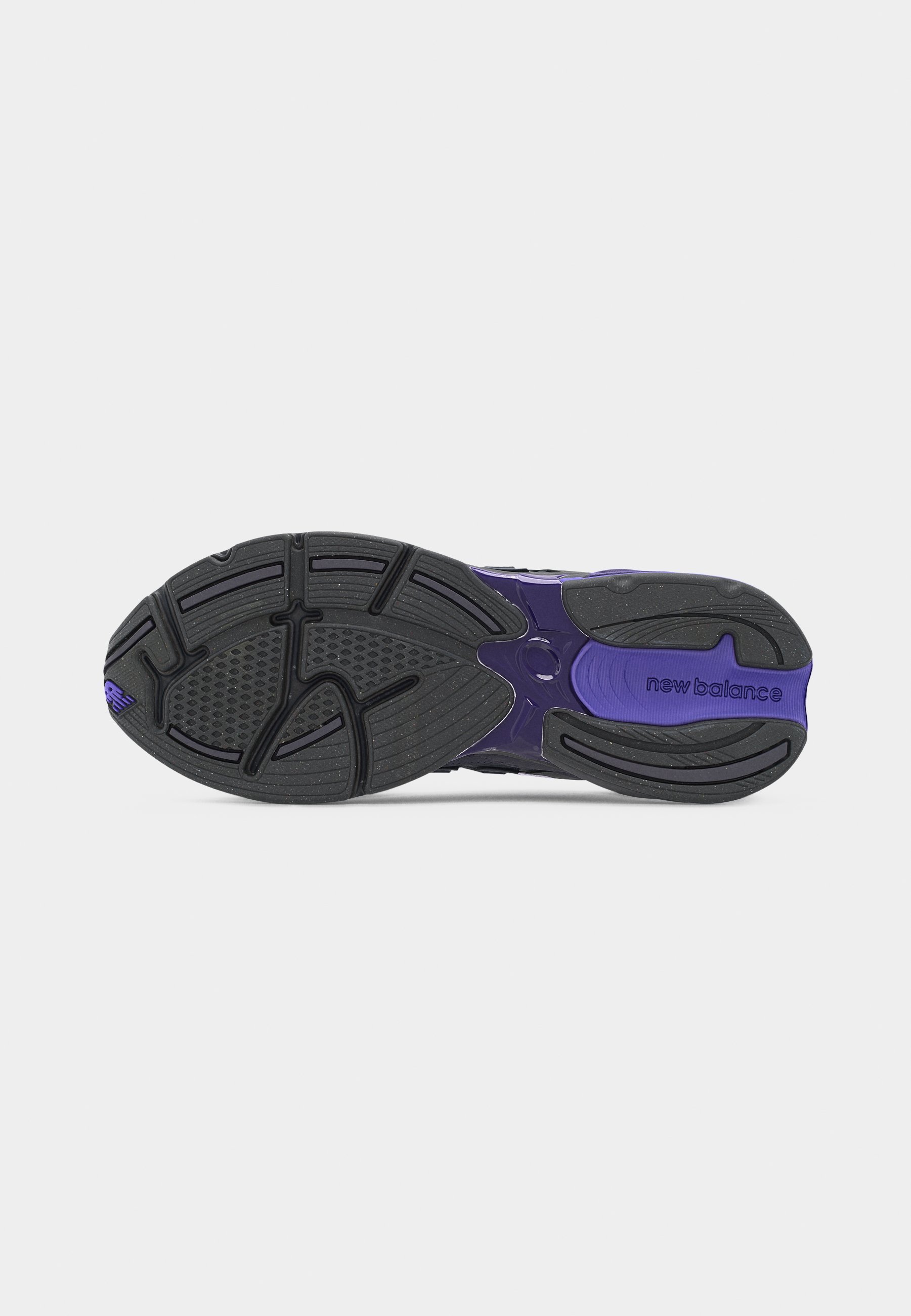 Suela de zapatilla New Balance en negro y morado con patrón de banda de rodadura texturizado y nombre de la marca visible en el área del talón.