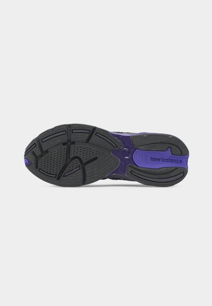 Suela de zapatilla New Balance en negro y morado con patrón de banda de rodadura texturizado y nombre de la marca visible en el área del talón.