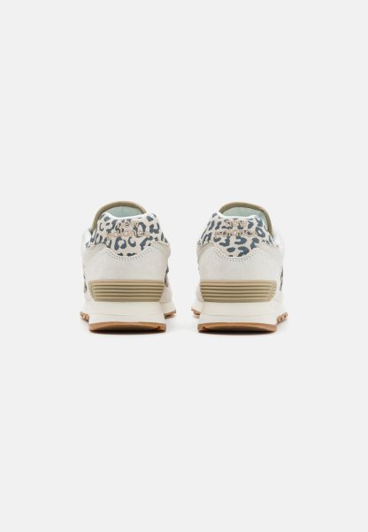 Par de zapatillas beige y blancas con detalle de estampado de leopardo en los cuellos de talón, medias suelas beige y suelas exteriores color chicle, mostradas desde atrás.