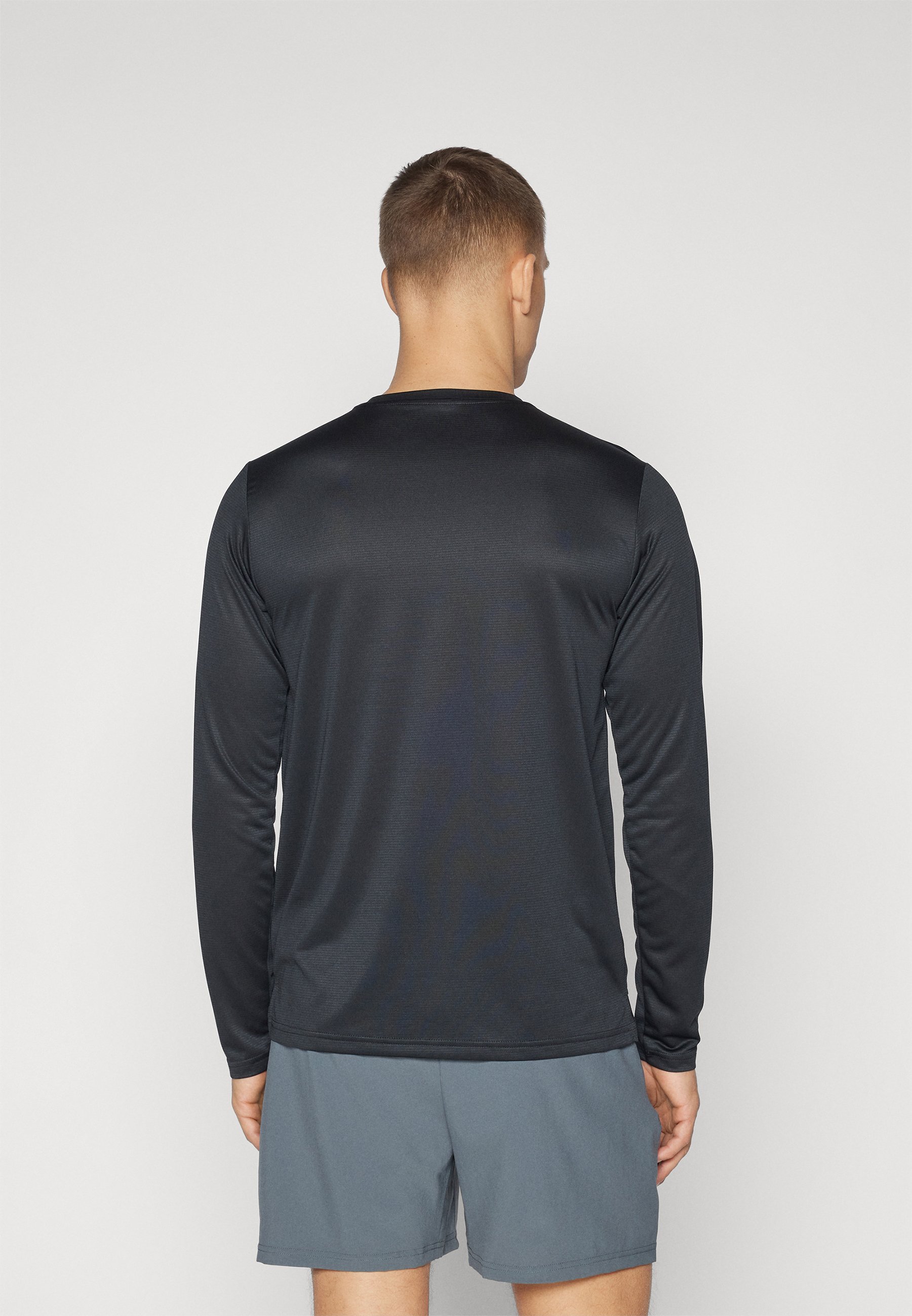 Camisa atlética larga negra de manga larga, hecha de un tejido suave y ligero; cuenta con un cuello redondo y se combina con pantalones cortos grises.
