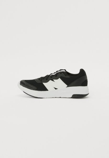 Zapatilla deportiva negra con parte superior de malla, logo blanco, cuello acolchado y suela de goma texturada. Cuenta con cierre de cordones y puntera reforzada.