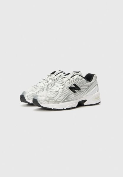 Par de zapatillas de correr New Balance blancas y plateadas con logo negro y suelas negras sobre un fondo claro.