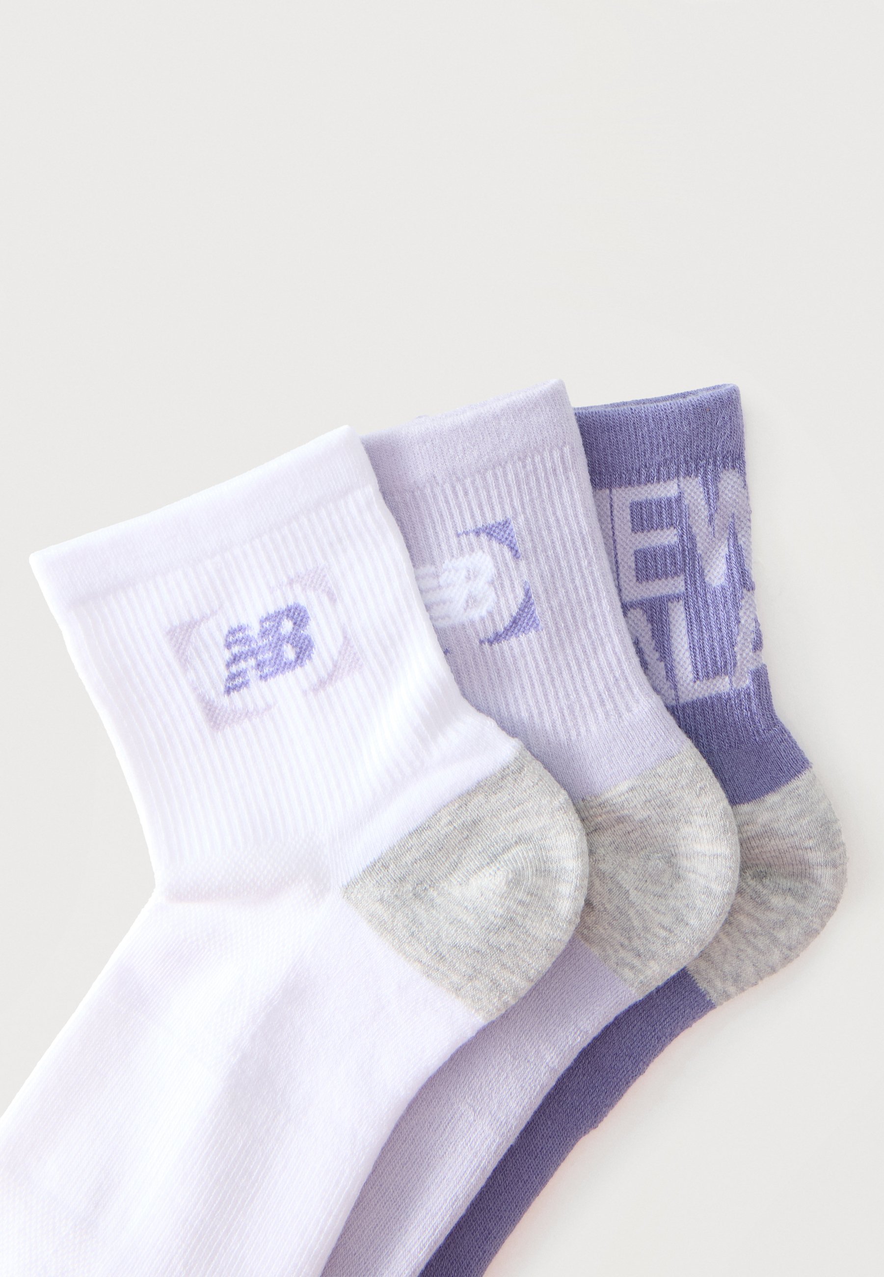 Tres calcetines de New Balance tipo crew en blanco, púrpura claro y púrpura oscuro con talones grises, apilados y ligeramente superpuestos.