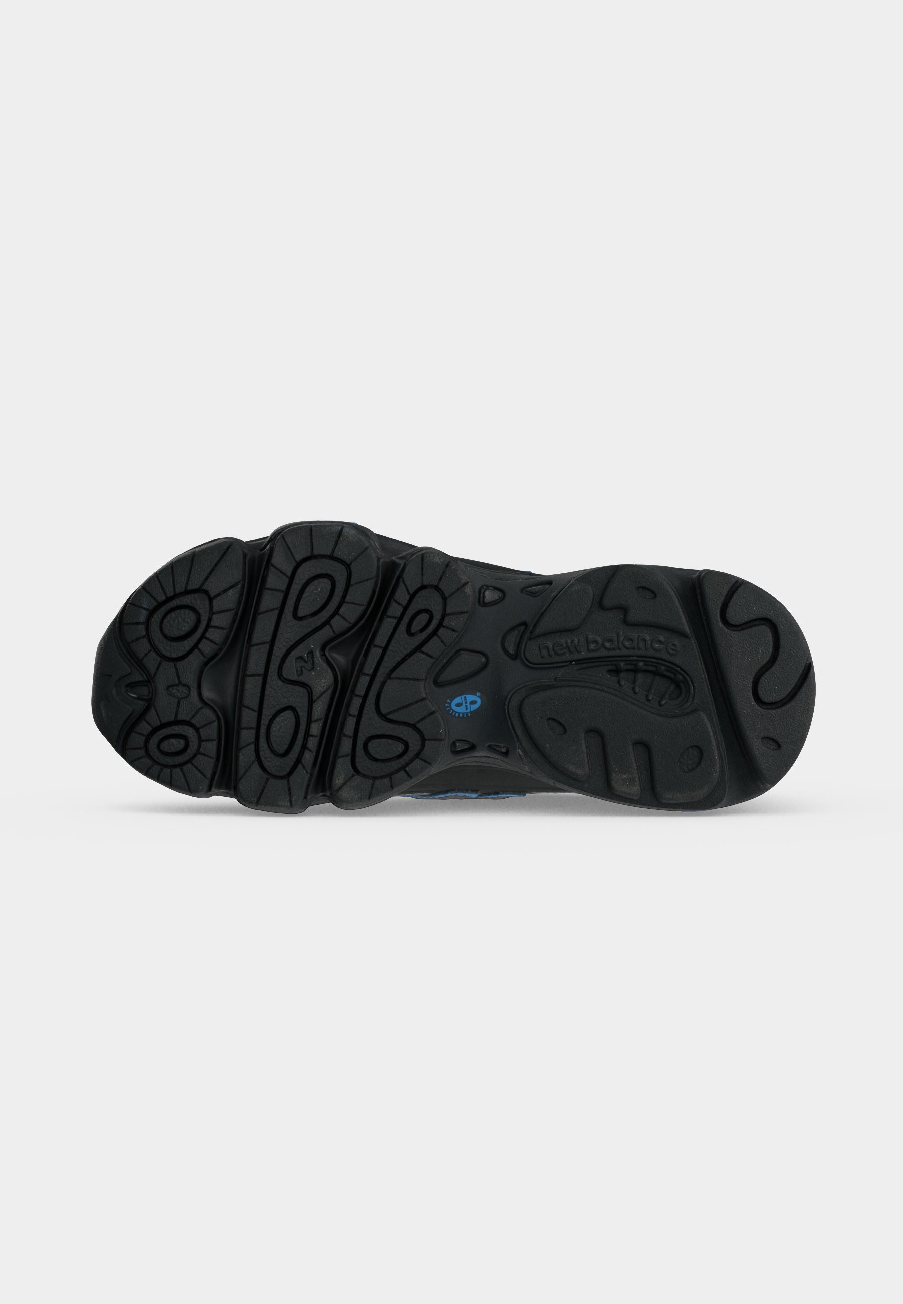 Suela negra de zapato New Balance con surcos profundos con patrones circulares y ondulados y un pequeño logo azul cerca del centro.