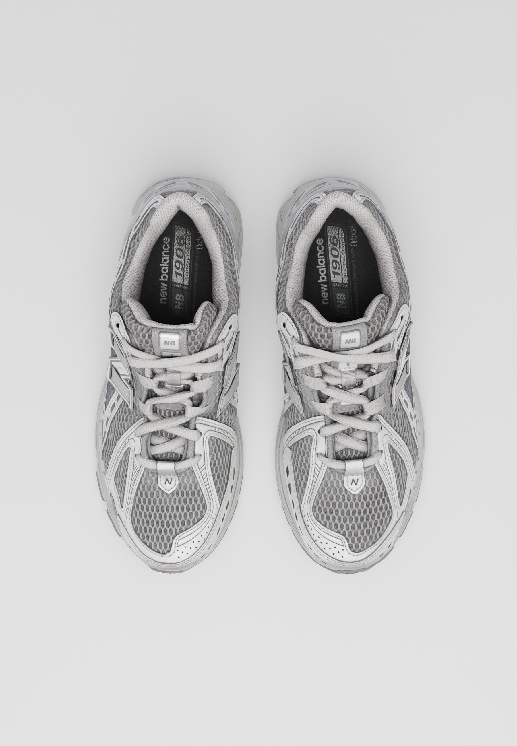 Zapatillas deportivas grises con parte superior de malla y sintético, cordones, cuello acolchado y suela de goma. Presenta detalles en gris claro y características de ventilación.
