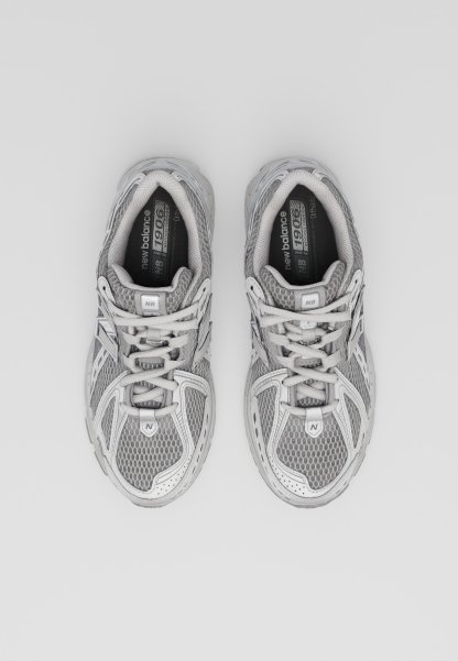Zapatillas deportivas grises con parte superior de malla y sintético, cordones, cuello acolchado y suela de goma. Presenta detalles en gris claro y características de ventilación.